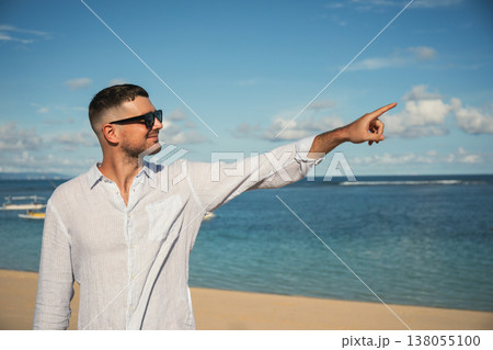 Man points towards the ocean while standing on sandy beach 138055100