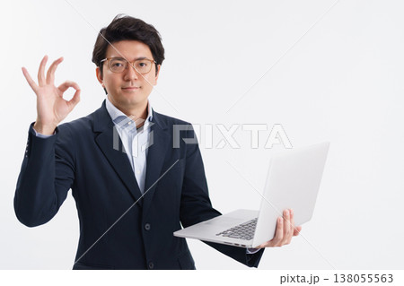 白背景の前でパソコンを持って指でOKを作るスーツ姿の30代の男性 138055563