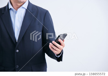 白背景の前で正面に立ちスマートフォンを手にした顔無しのスーツ姿の男性 138055572