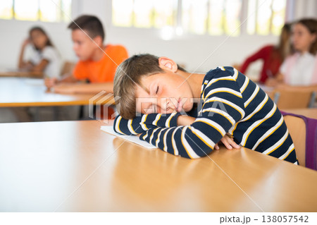 Bored tween schoolboy sleeping at desk in classroom during lesson Bored tween schoolboy sleeping at desk in classroom during lesson 138057542