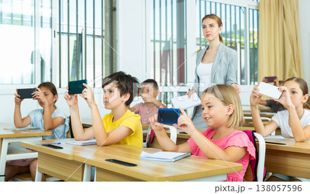 Absorbed preteen school children using mobile phones at lesson Absorbed preteen school children using mobile phones at lesson 138057596
