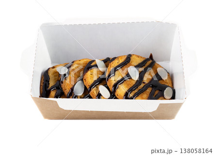Freshly baked sweet cookies with chocolate drizzle and almond flakes in craft paper take out container on white background side view with copy space 138058164