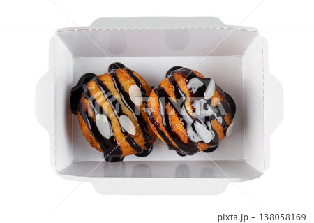 Sweet choux pastry with chocolate sauce and almond flake in white paper take out box on white background top view close up flat lay with copy space Sweet choux pastry with chocolate sauce and almond flake in white paper take out box on white background top view close up flat lay with copy space 138058169