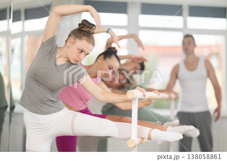 Teen ballet students prepare for classes, near ballet bare stretch legs under man teacher guidance Teen ballet students prepare for classes, near ballet bare stretch legs under man teacher guidance 138058861