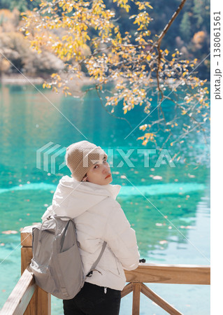 Happy woman traveler travel in jiuzhaigou national park in Sichuan, China. Tourist sightseeing Five Flower lake and snow mountain in Autumn season. Famous Landmark and Vacation near Chengdu, China 138061561