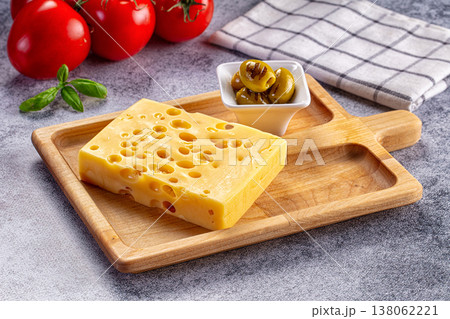 Block of Swiss cheese on a wooden cutting board with grilled olives and fresh tomatoes 138062221