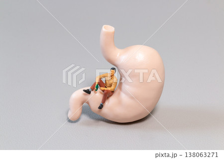 Miniature Man Sitting on Stomach Model Holding Bottle Symbolizing Alcohol Impact on Digestive System Miniature Man Sitting on Stomach Model Holding Bottle Symbolizing Alcohol Impact on Digestive System 138063271