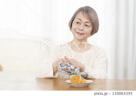 リビングでおやつを食べながらお茶を飲むシニア女性 リビングでおやつを食べながらお茶を飲むシニア女性 138063395