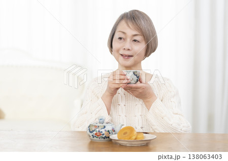 リビングでおやつを食べながらお茶を飲むシニア女性 リビングでおやつを食べながらお茶を飲むシニア女性 138063403