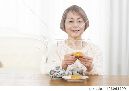 リビングでおやつを食べながらお茶を飲むシニア女性 リビングでおやつを食べながらお茶を飲むシニア女性 138063409