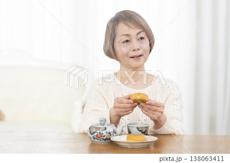 リビングでおやつを食べながらお茶を飲むシニア女性 リビングでおやつを食べながらお茶を飲むシニア女性 138063411