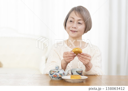 リビングでおやつを食べながらお茶を飲むシニア女性 リビングでおやつを食べながらお茶を飲むシニア女性 138063412