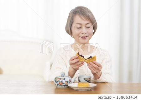 リビングでおやつを食べながらお茶を飲むシニア女性 リビングでおやつを食べながらお茶を飲むシニア女性 138063414