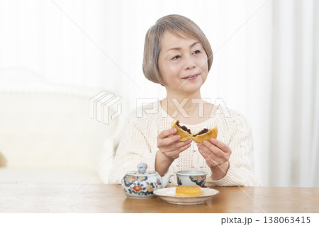 リビングでおやつを食べながらお茶を飲むシニア女性 リビングでおやつを食べながらお茶を飲むシニア女性 138063415