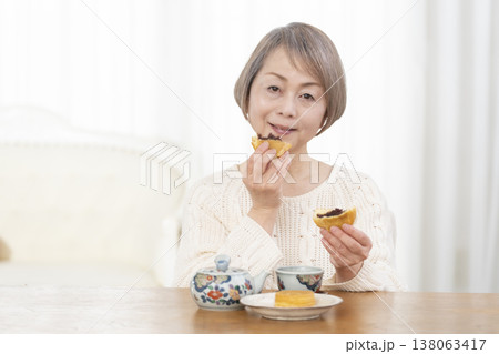 リビングでおやつを食べながらお茶を飲むシニア女性 リビングでおやつを食べながらお茶を飲むシニア女性 138063417