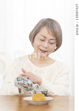 リビングでおやつを食べながらお茶を飲むシニア女性 リビングでおやつを食べながらお茶を飲むシニア女性 138063425