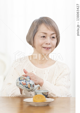 リビングでおやつを食べながらお茶を飲むシニア女性 リビングでおやつを食べながらお茶を飲むシニア女性 138063427