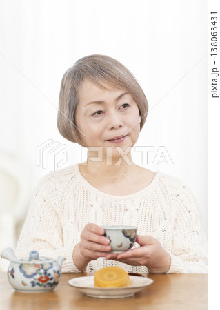 リビングでおやつを食べながらお茶を飲むシニア女性 リビングでおやつを食べながらお茶を飲むシニア女性 138063431