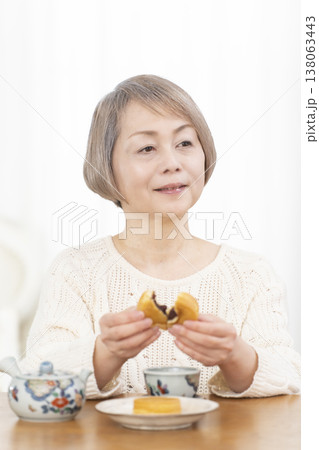 リビングでおやつを食べながらお茶を飲むシニア女性 リビングでおやつを食べながらお茶を飲むシニア女性 138063443