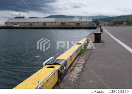 小樽港のコンクリート岸壁にある黄色の安全縁石。曇り空の下の海の風景 小樽港のコンクリート岸壁にある黄色の安全縁石。曇り空の下の海の風景 138063889
