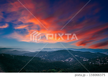 Fiery dramatic sunset sky over dark forested mountains near Barcelona 138066375