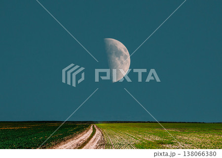 Giant half moon over green field and rural dirt road 138066380