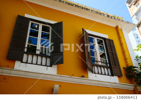 Colorful yellow Portuguese colonial building facade with dark shuttered windows and blue sky in Macau Colorful yellow Portuguese colonial building facade with dark shuttered windows and blue sky in Macau 138066411