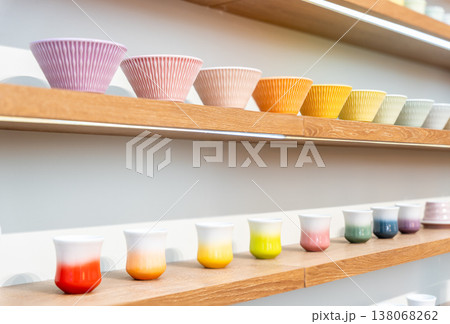 Variety of colorful ceramic pottery bowls and Japanese tea cup mugs displayed on wooden shelves. 138068262