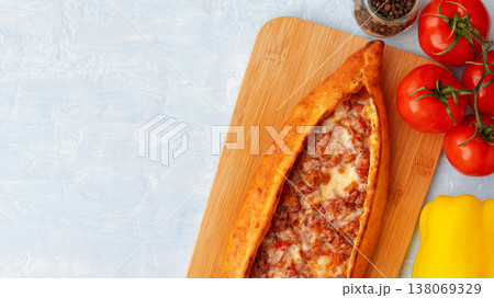 Delicious Turkish pide with cheese and toppings on a wooden board at kitchen table 138069329