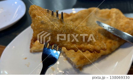 A person's hand a piece of pasty with a fork and lifts it up to eat 138069330