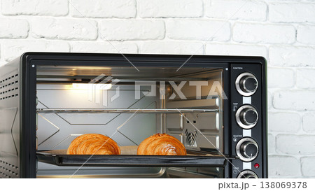 Baking croissants in a toaster oven located in a modern kitchen with white brick wall Baking croissants in a toaster oven located in a modern kitchen with white brick wall 138069378