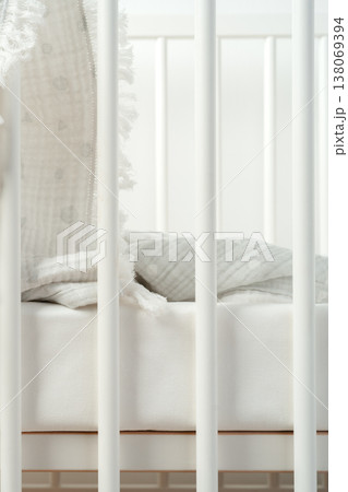 Baby crib with white bedding and soft blankets during daytime in a nursery setting Baby crib with white bedding and soft blankets during daytime in a nursery setting 138069394