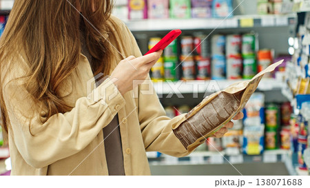 Woman Scanning Pet Food With Smartphone And Reading Ingredients And Product Information In Store Before Purchase. Smart Shopping And Informed Buying Decision Concept. Woman Scanning Pet Food With Smartphone And Reading Ingredients And Product Information In Store Before Purchase. Smart Shopping And Informed Buying Decision Concept. 138071688