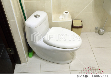 A white toilet bowl and beige ceramic tiles. A white toilet bowl and beige ceramic tiles. 138072644