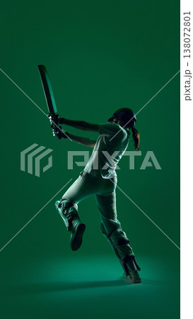 Female cricket batter from back view swinging bat in powerful motion on green background. Female cricket batter from back view swinging bat in powerful motion on green background. 138072801