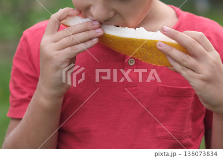 A moment of delight as a boy tastes a ripe melon, his face a picture of satisfaction. This image speaks to the importance of incorporating fruit into daily nutrition. 138073834