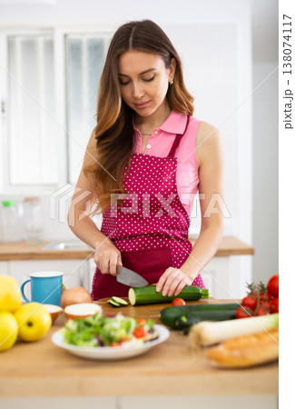 Smiling young woman preparing vegetable salad in home kitchen 138074117