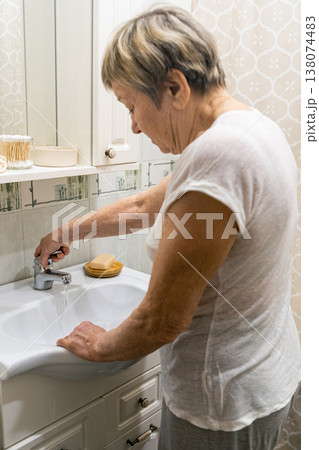 Senior woman turning on faucet, preparing to wash hands in bathroom sink. Emphasizing daily self-care and cleanliness, hygiene routine. The real life of an elderly person, daily routine Senior woman turning on faucet, preparing to wash hands in bathroom sink. Emphasizing daily self-care and cleanliness, hygiene routine. The real life of an elderly person, daily routine 138074483