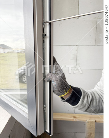 A man wearing gloves adjusts plastic windows with a screwdriver. Installation and adjustment of plastic windows in a private house. 138074647