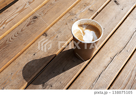 Latte or cappuccino with plant milk in beige paper cup on wooden striped table outside, drinking coffee, light and shadow . Latte or cappuccino with plant milk in beige paper cup on wooden striped table outside, drinking coffee, light and shadow . 138075105