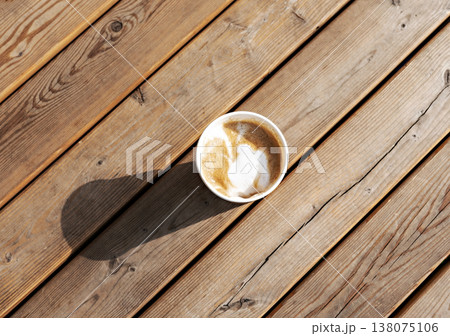 Latte or cappuccino with plant milk in beige paper cup on wooden striped table outside, drinking coffee, light and shadow . 138075106