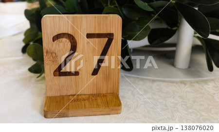 close up of a wooden stand sign with the number 27 written on it. Plants at the back on a white table with copy space close up of a wooden stand sign with the number 27 written on it. Plants at the back on a white table with copy space 138076020