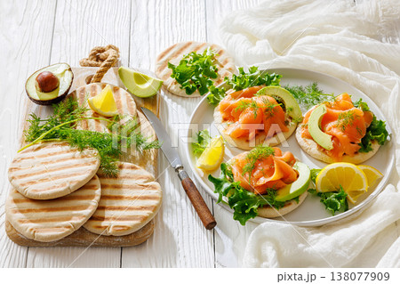 open-faced grilled pita sandwiches with lettuce, smoked salmon slices, avocado, dill, and lemon wedges  138077909