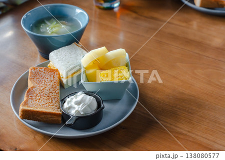木のテーブルに並ぶトーストとたまごサンドとヨーグルトとフルーツとスープの朝食セット 138080577