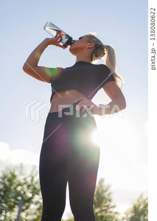 Woman exercising outdoors while hydrating and monitoring fitness data in sunlight Woman exercising outdoors while hydrating and monitoring fitness data in sunlight 138080622