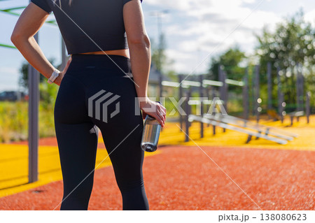 Fitness enthusiast resting at outdoor gym with water bottle during workout 138080623