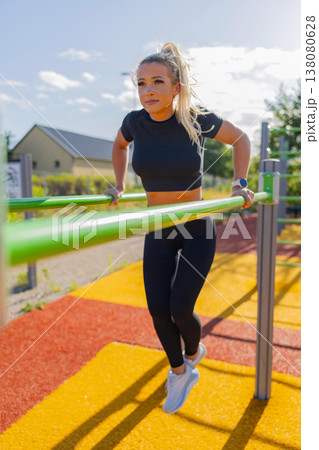 Woman exercising on parallel bars in outdoor fitness area on a sunny day Woman exercising on parallel bars in outdoor fitness area on a sunny day 138080628