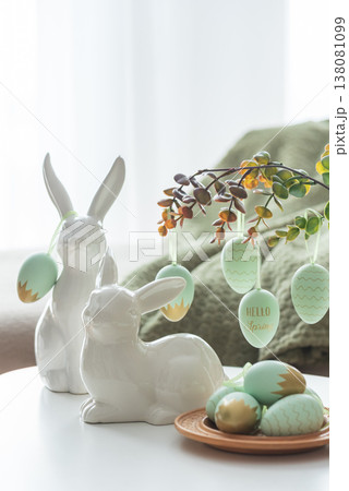 Cozy Easter Living Room Decor with Bunny Figurines and Hanging Eggs on White Table 138081099