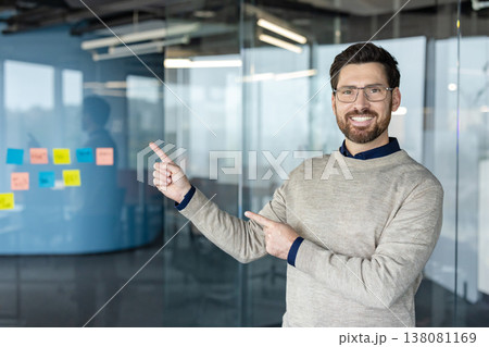 Smiling man pointing with both hands, presenting new ideas and a business strategy with colorful sticky notes on a glass wall in a modern office workplace Smiling man pointing with both hands, presenting new ideas and a business strategy with colorful sticky notes on a glass wall in a modern office workplace 138081169