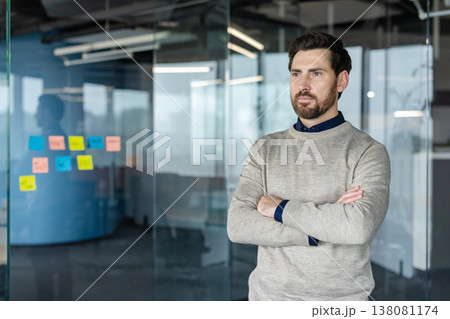 Confident businessman with arms crossed, looking away thoughtfully in a modern glass office, planning strategy and envisioning growth for a startup or corporate team Confident businessman with arms crossed, looking away thoughtfully in a modern glass office, planning strategy and envisioning growth for a startup or corporate team 138081174